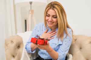 Free photo young happy surprised woman with gift box on sofa
