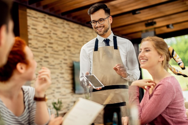 Young happy waiter taking order from his guests in a cafe