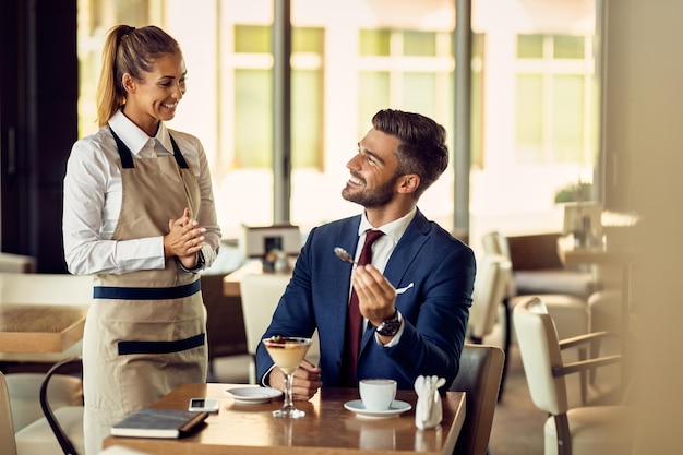 Young happy waitress talking to a businessman in a cafe