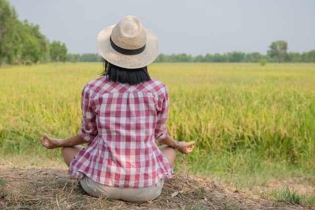 タイ、アジアの棚田の美しい景色を楽しみ、瞑想している若い幸せな女性。旅行写真。ライフスタイル。屋外の田んぼに座ってヨガのリラクゼーションを練習している女性。