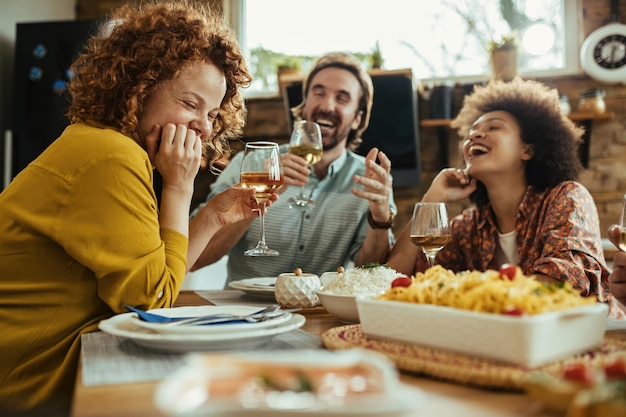 Молодая счастливая женщина и ее друзья веселятся, попивая вино во время обеда дома