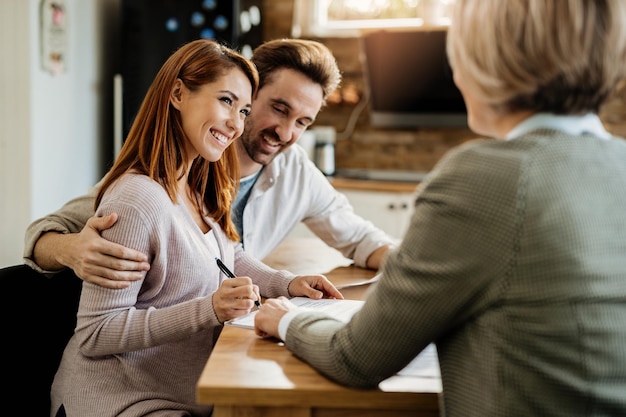 Young happy woman and her husband signing an agreement with insurance agent during a meeting