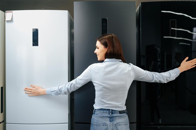 Молодая счастливая женщина, опираясь на свой новый холодильник в торговом центре
