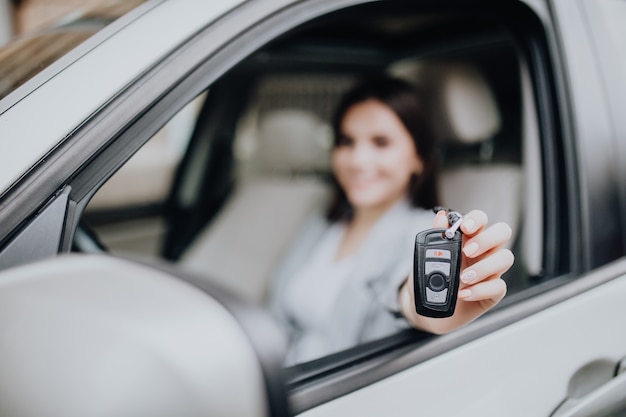 手に鍵を持って車の近くの若い幸せな女性。車を買うというコンセプト。キーに焦点を当てます。