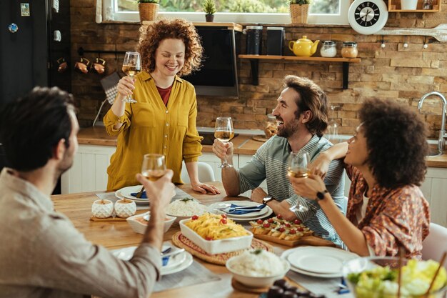Молодая счастливая женщина произносит тост во время обеда со своими друзьями дома