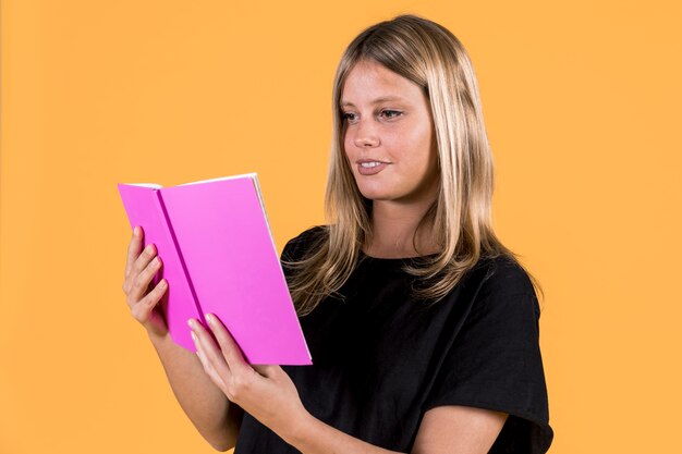 Young happy woman reading book on yellow background