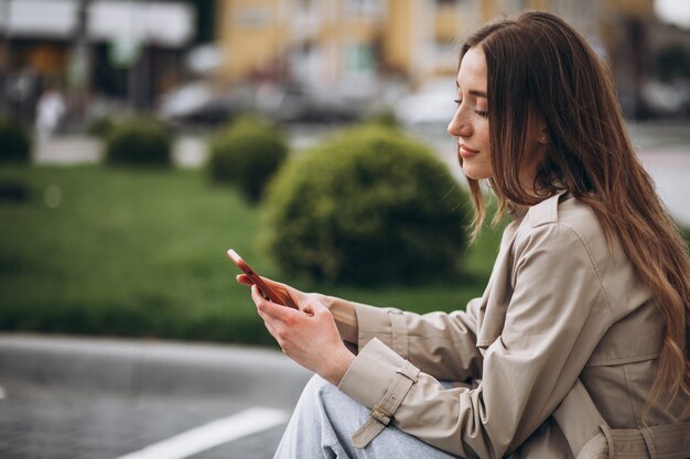 Young happy woman sitting in park and talking on the phone