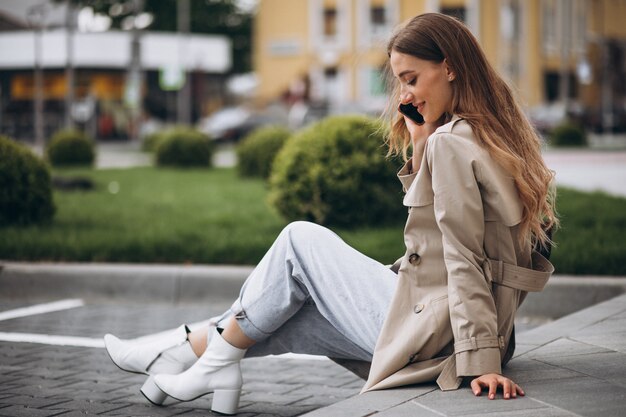 Молодая счастливая женщина сидит в парке и разговаривает по телефону