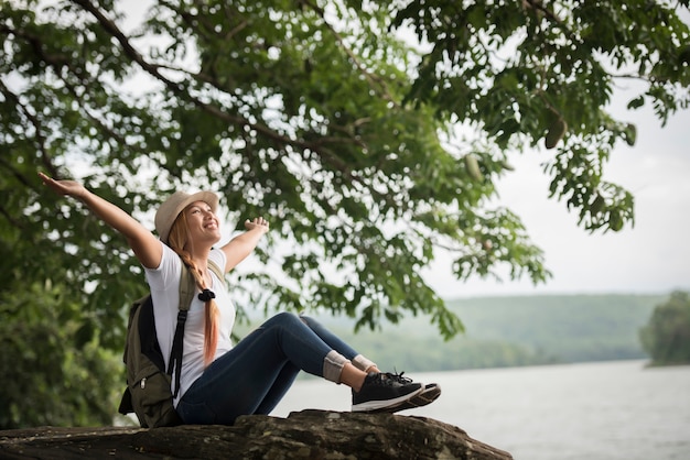 バックパックで座っている若い幸せな女性はハイキングの後で自然を楽しむ。