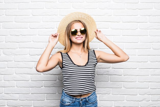 Free photo young happy woman smiling in sunglasses and summer hat over white brick wall