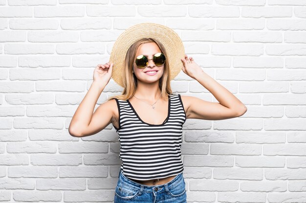 흰색 벽돌 벽 위에 선글라스와 여름 모자에 웃 고 젊은 행복 한 여자