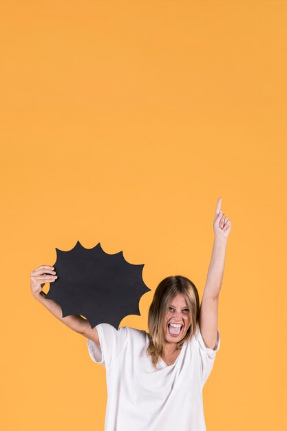 Young happy woman with mouth open holding black speech bubble and pointing up