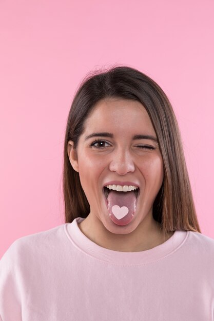 Young happy woman with ornament heart on tongue 