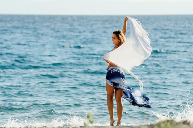 여름 방학 동안 해변에서 즐거운 시간을 보내는 숄을 두른 젊은 행복한 여자