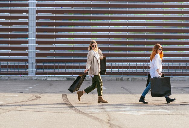 Молодые счастливые женщины с хозяйственными сумками, идущими по улице.