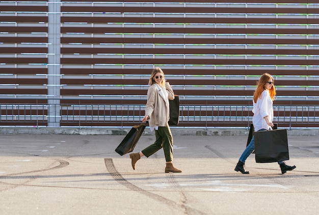 Young happy women with shopping bags walking on street.