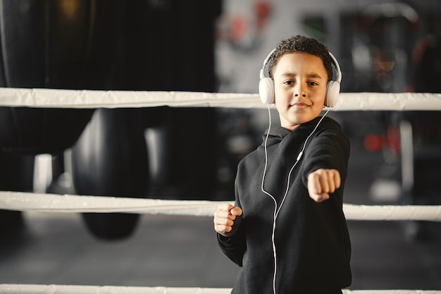 Молодой трудолюбивый боксер учится боксировать. Ребенок в спортивном центре. Малыш с наушниками.