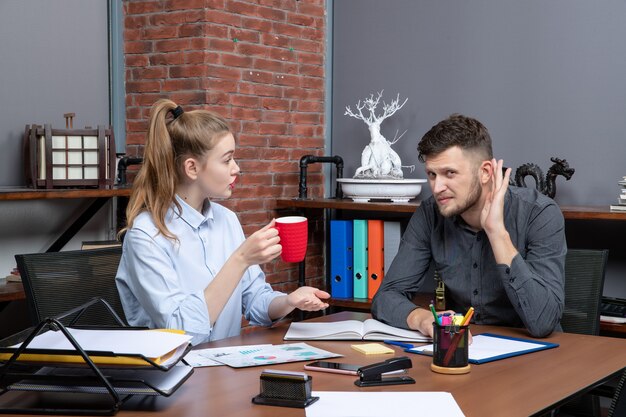 Young harworking female worker and her male co-worker sitting at the table discussing one important issue in the office