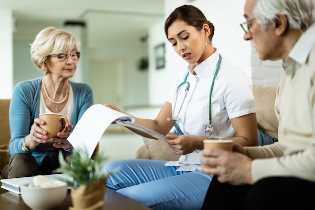 Free photo young healthcare worker and senior couple analyzing medical test results during home visit