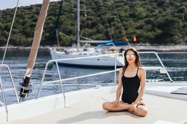 Young healthy and calm woman doing yoga on sailing yacht boat in sea at island 