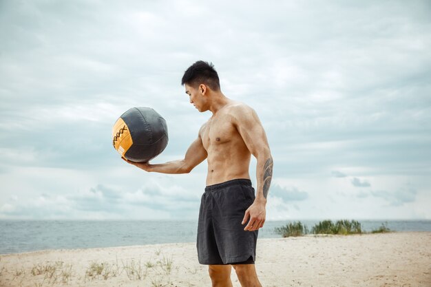 Young healthy man athlete doing exercise with ball at the beach