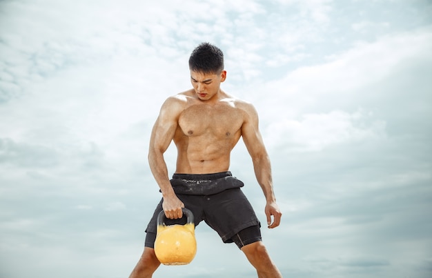 Young healthy man athlete doing exercise with the weight at the beach