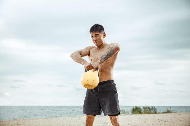 Young healthy man athlete doing exercise with the weight at the beach