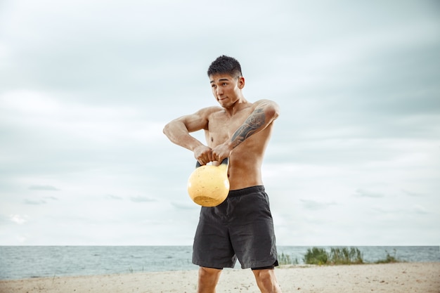 Молодой здоровый спортсмен-мужчина делает упражнения с весом на пляже