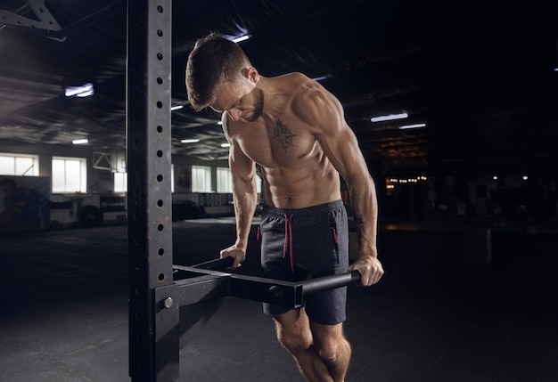 Free photo young healthy man, athlete doing exercises, pull-ups in gym