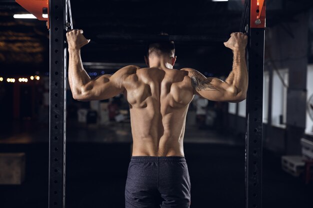 Young healthy man, athlete doing exercises, pull-ups in gym