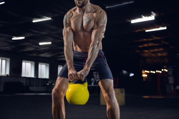 Young healthy man, athlete doing exercises with the weight in gym. Single caucasian model practicing hard, training his body. Concept of healthy lifestyle, sport, fitness, bodybuilding, wellbeing.