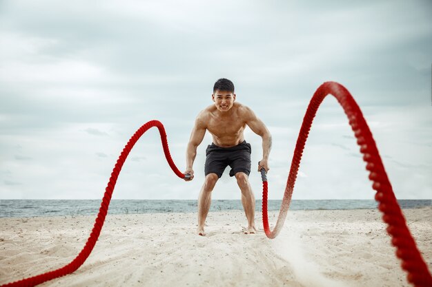 Young healthy man athlete doing squats at the beach