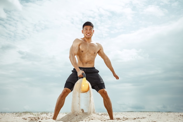 Молодой здоровый человек-спортсмен делает приседания на пляже