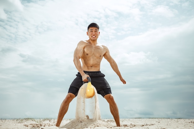 Young healthy man athlete doing squats at the beach