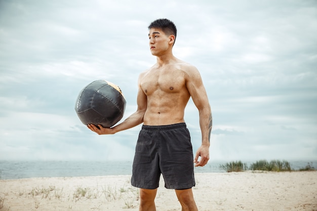 Free photo young healthy man athlete doing squats at the beach