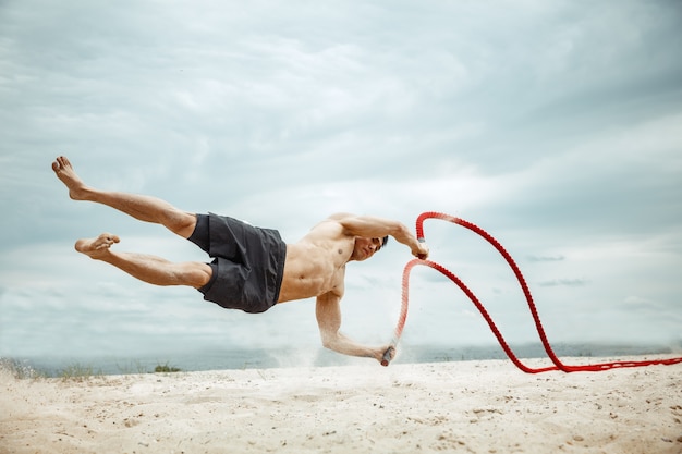 Young healthy man athlete doing squats at the beach