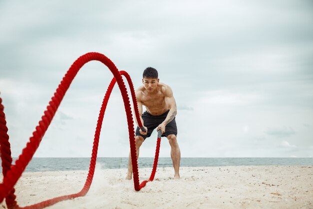 Young healthy man athlete doing squats at the beach