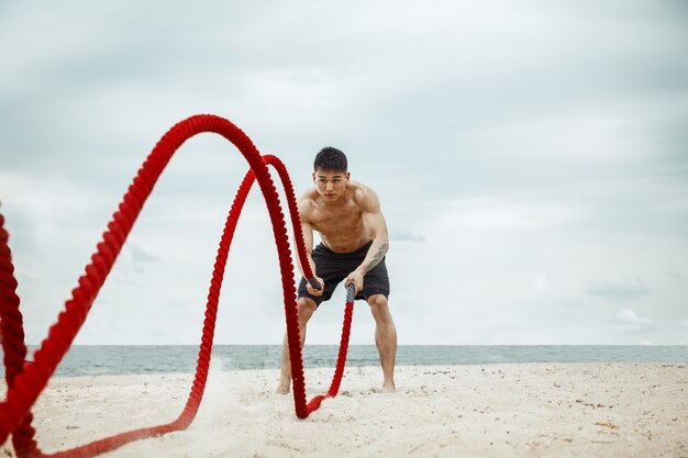 Молодой здоровый человек-спортсмен делает приседания на пляже