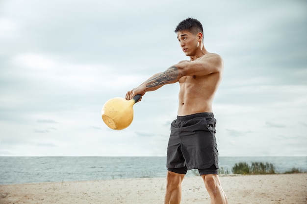 Free photo young healthy man athlete doing squats at the beach