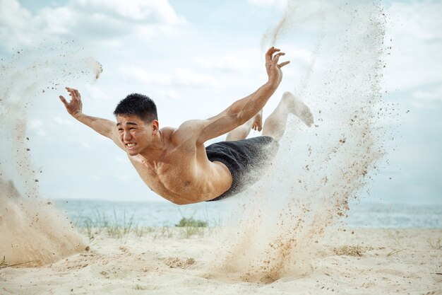 Young healthy man athlete doing squats at the beach