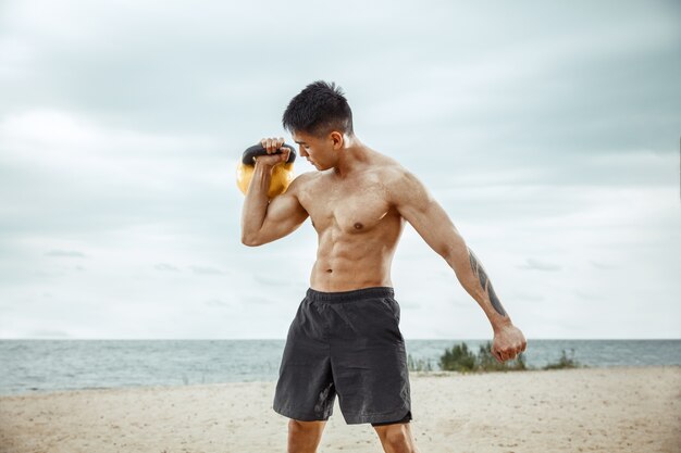Young healthy man athlete doing squats at the beach