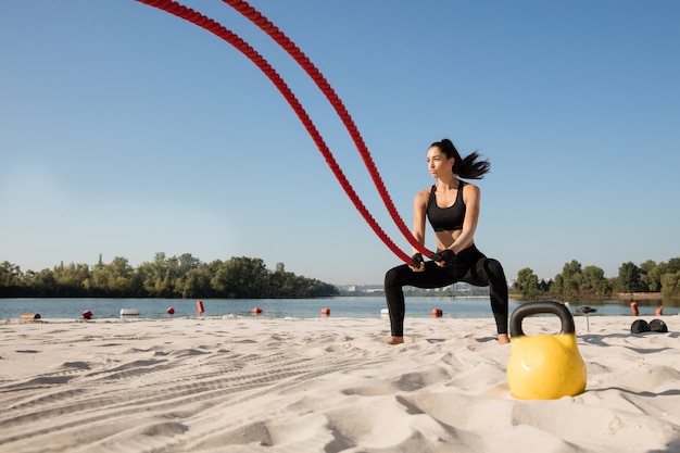 Young healthy woman doing exercise with the ropes at the beach.