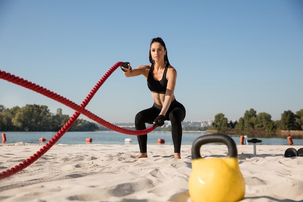 Giovane donna in buona salute che fa esercizio con le corde in spiaggia