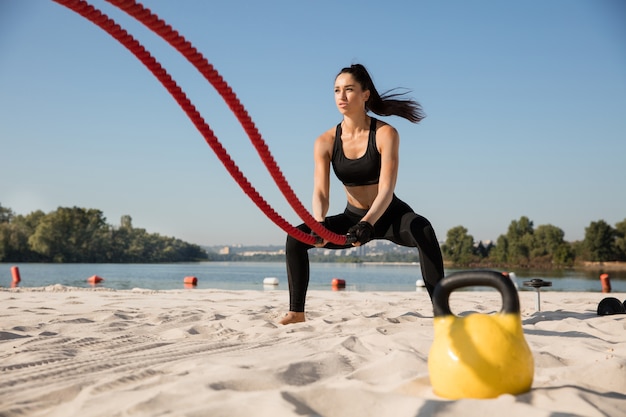 Young healthy woman doing exercise with the ropes at the beach