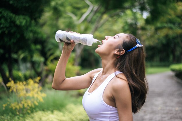 ジョギングの後、プラスチック製のボトルから若い健康的な女性の飲み水。