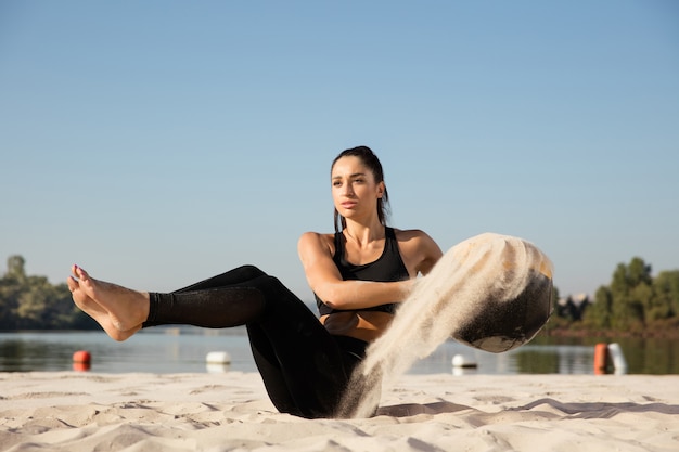 Young healthy woman training upper body with ball at the beach