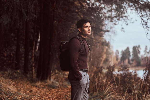 A young hiker with a backpack wearing sweater enjoying a walk in the autumn forest.
