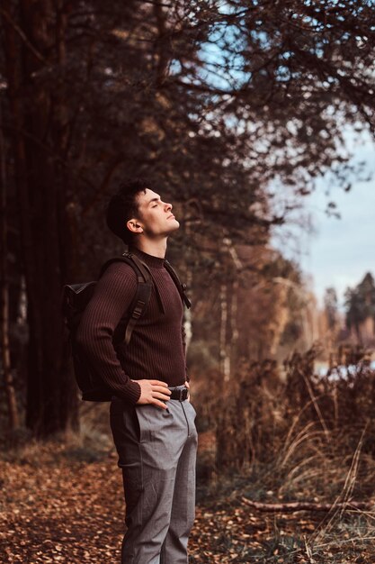 A young hiker with a backpack wearing sweater enjoying a walk in the autumn forest.