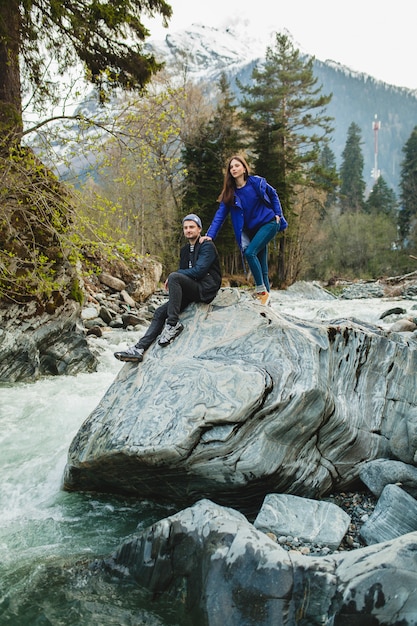 冬の森の川で岩の上を歩く愛の流行に敏感な若い美しいカップル