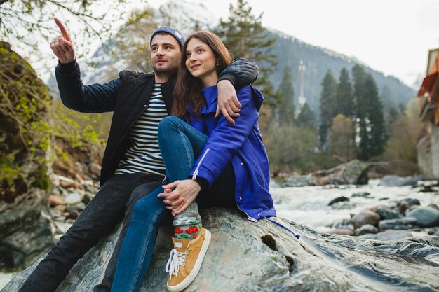 Young hipster beautiful couple in love walking on a rocks at river in winter forest